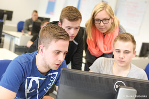 Vier junge Menschen sitzen vor einem Computer und bearbeiten etwas. 